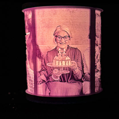 Lit birthday memory lamp showing a woman holding a cake with candles, with family photo panels visible around the curved shade.