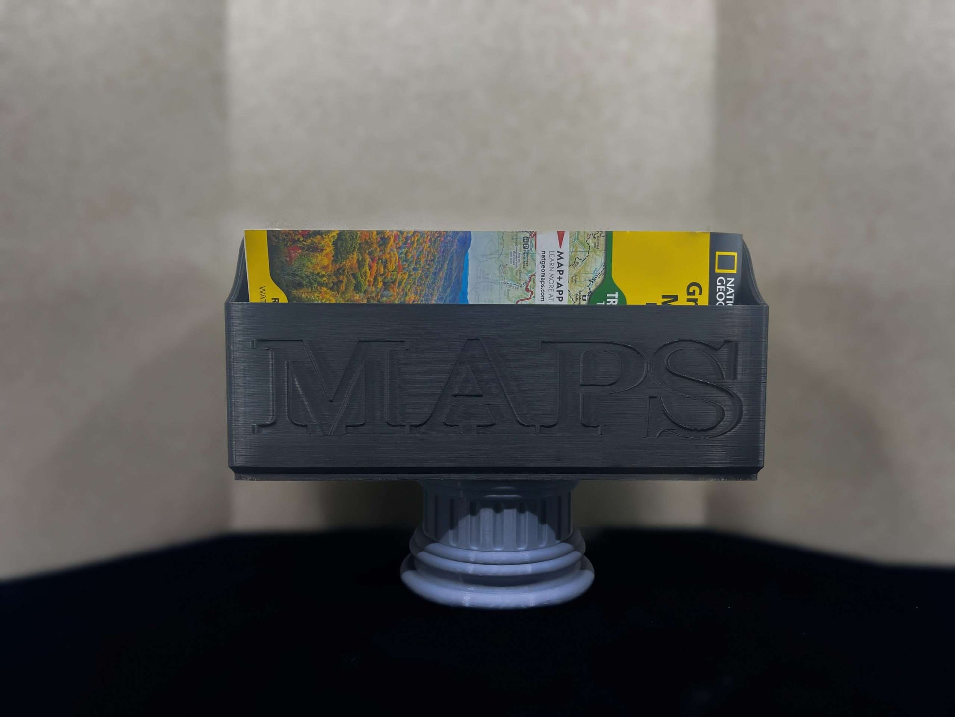 Black NatGeo Map Box holding maps on a gray pedestal