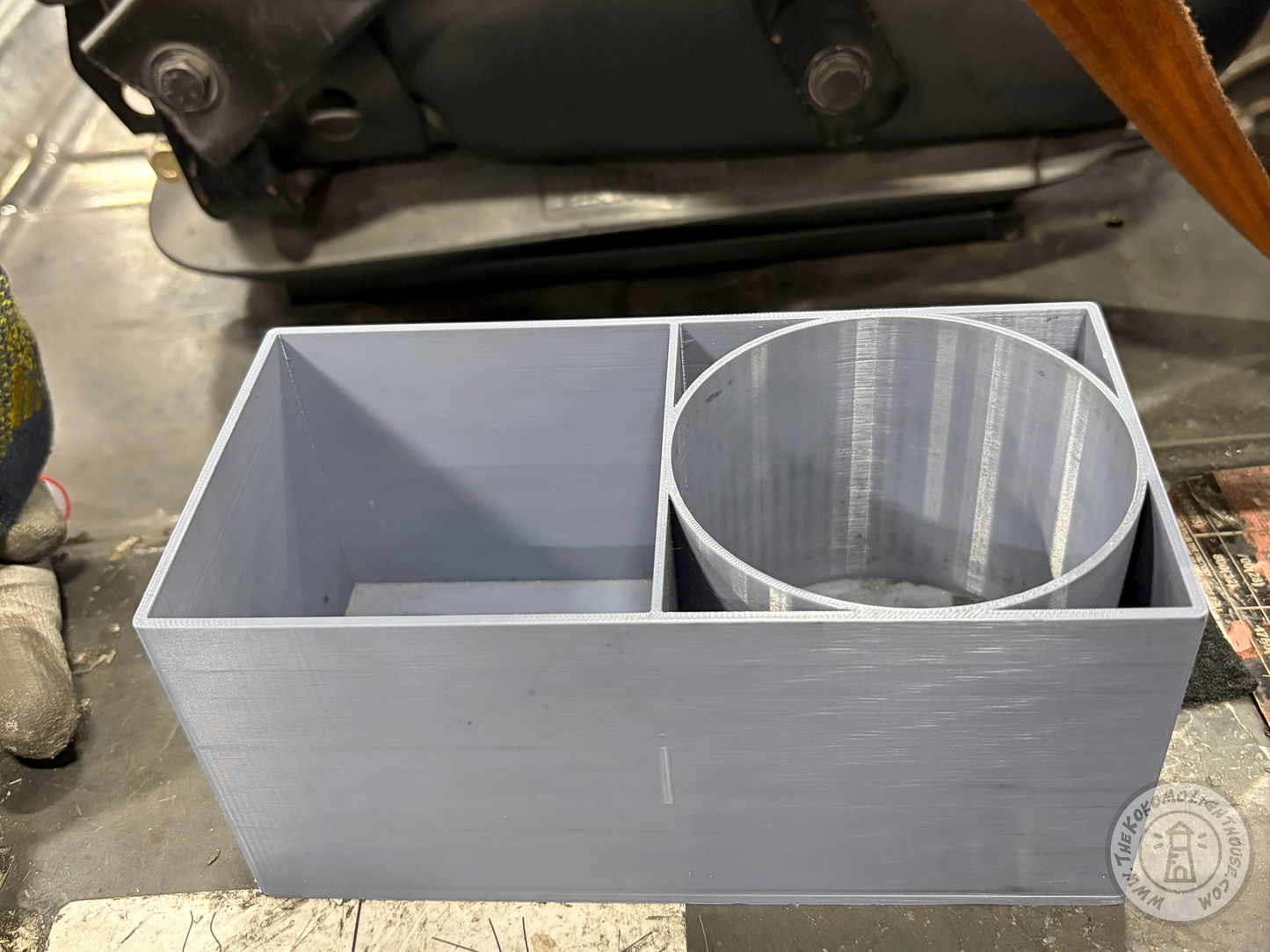 A light gray 3D-printed rectangular organizer box with a circular insert, photographed in a workshop environment on a fork truck.