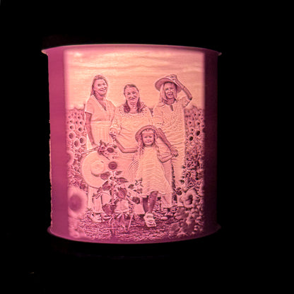 Lit personalized family lithophane lamp showing several family members and a child in a sunflower filled garden setting, with the image glowing through the shade.