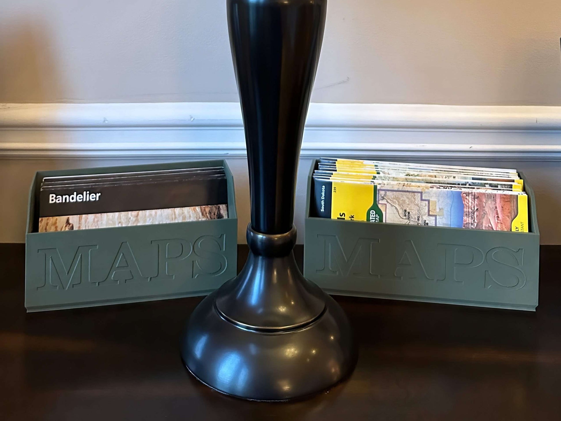 Green classic map box with unigrids next a Green NatGeo Map Box holding maps on a table next to a lamp base