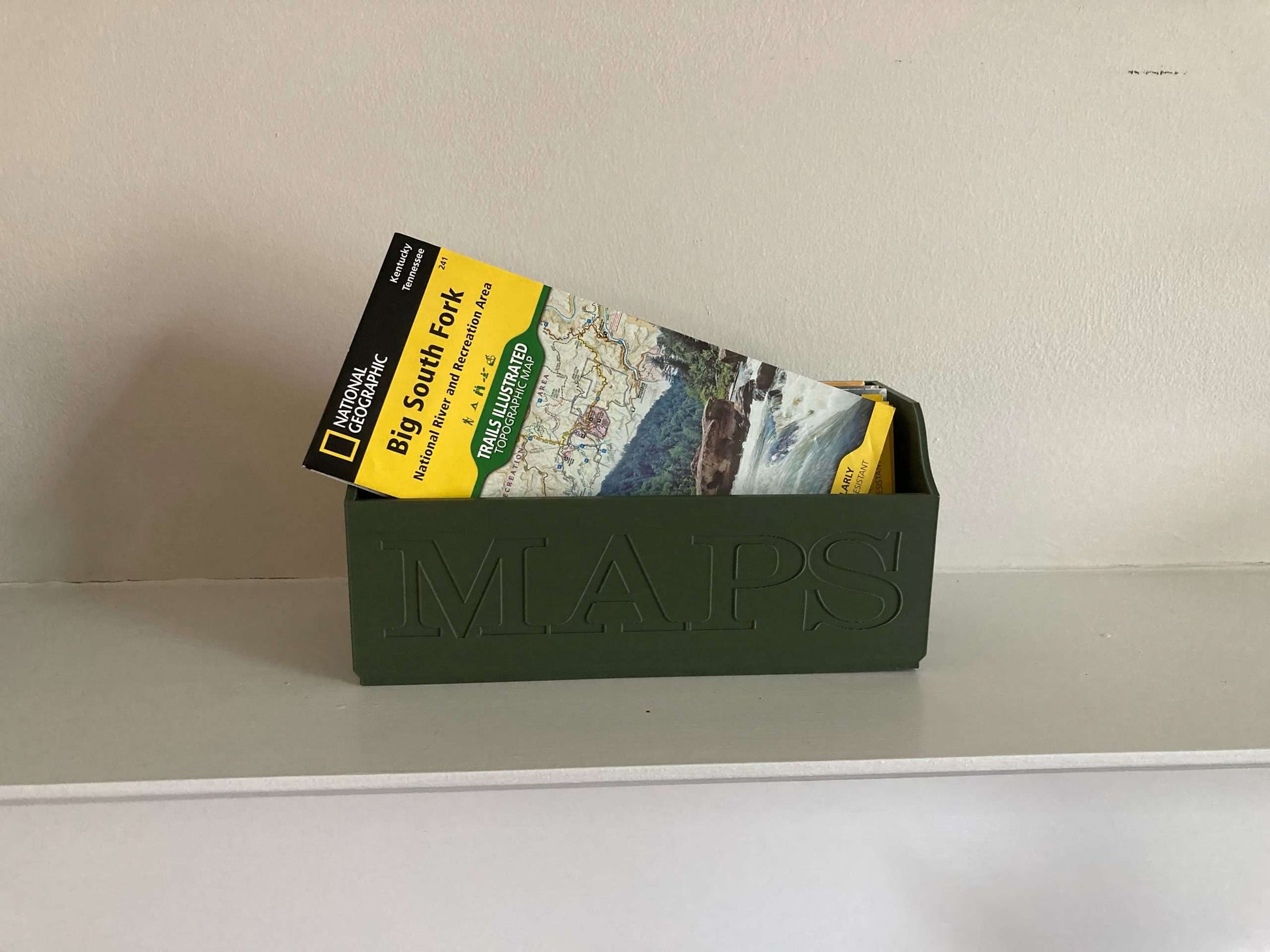 Green NatGeo Map Box holding maps on white shelf