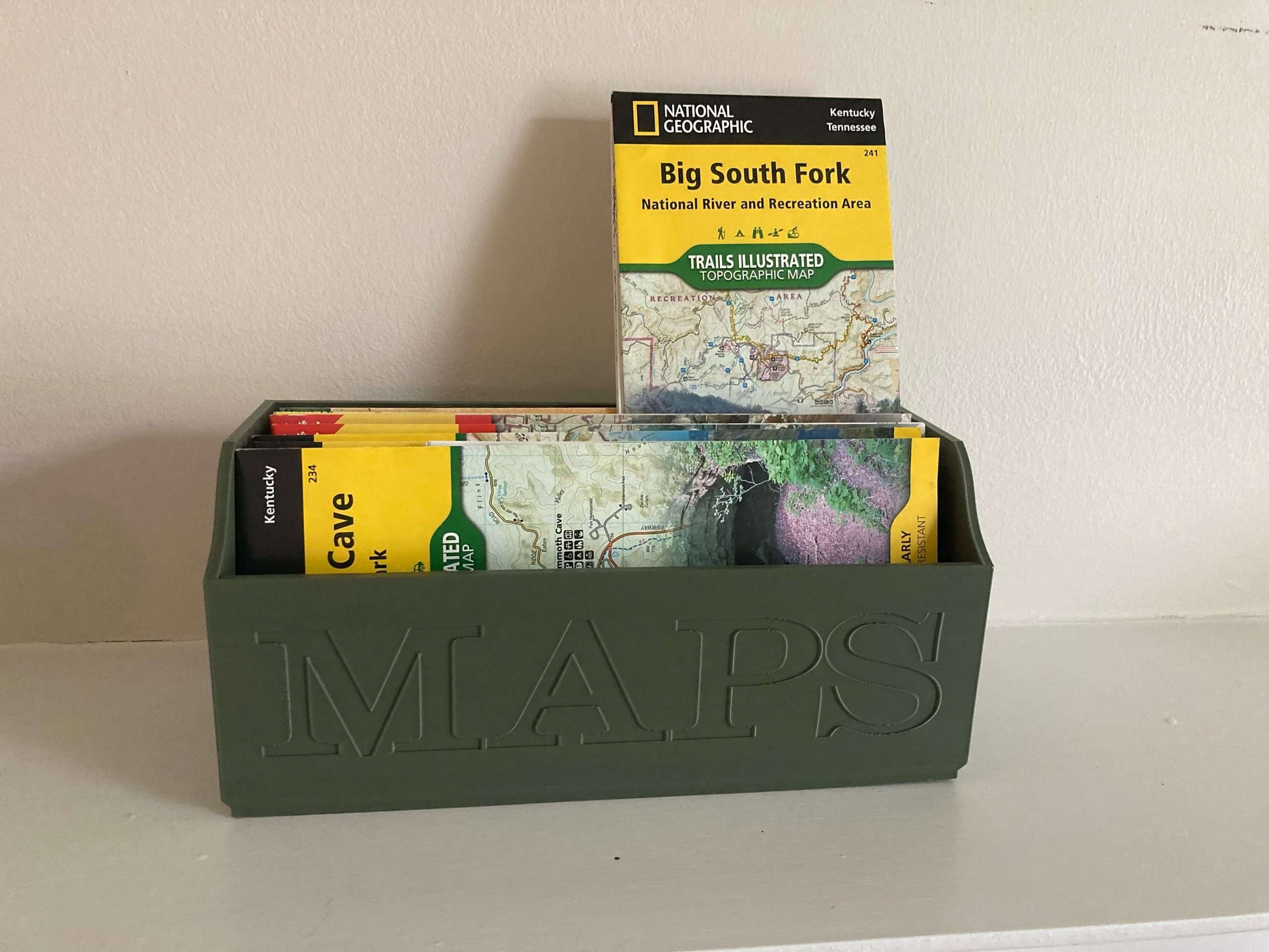 Green NatGeo Map Box holding maps on white shelf
