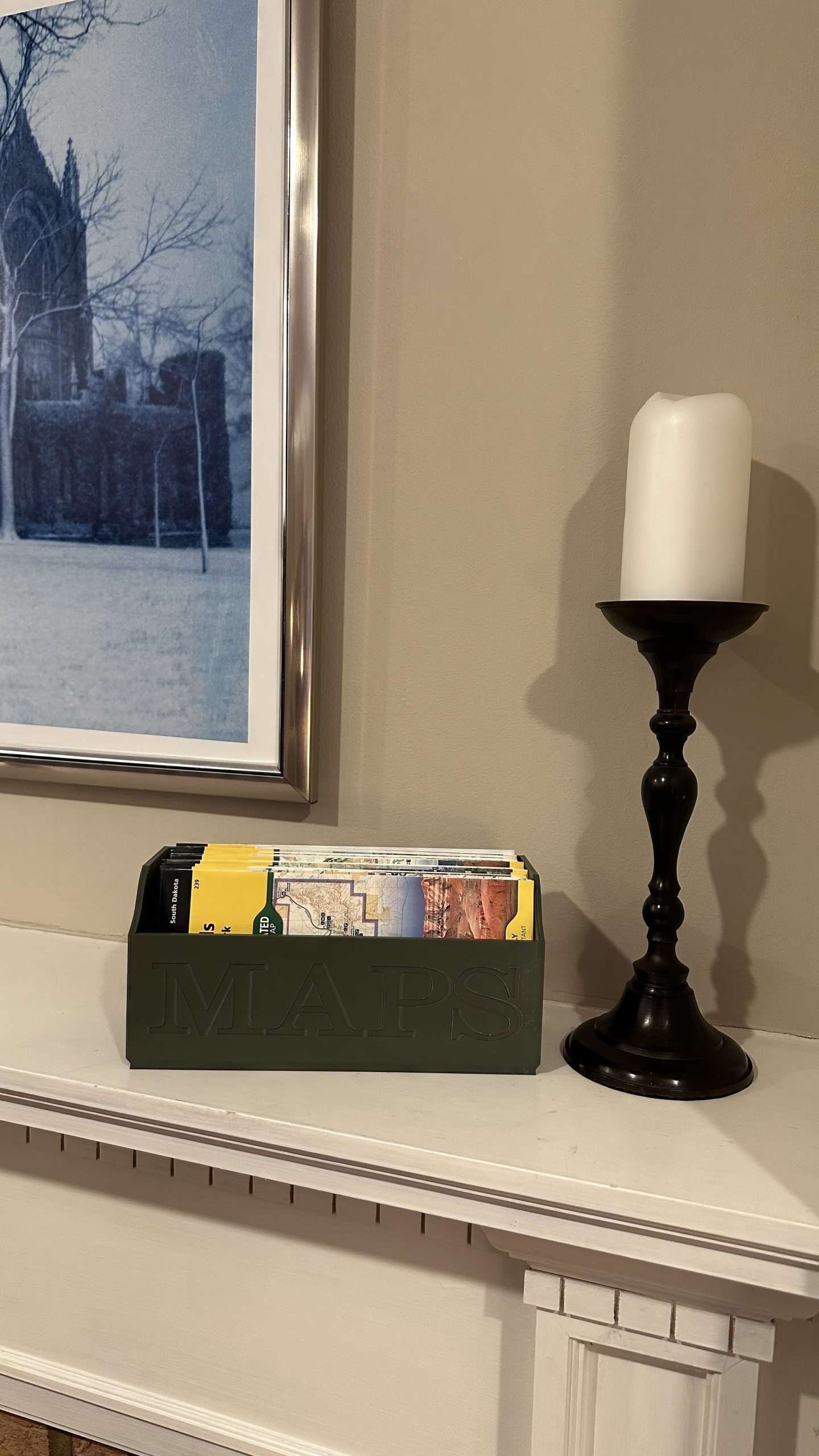Green NatGeo Map Box holding maps on white fireplace mantle next to candlestick