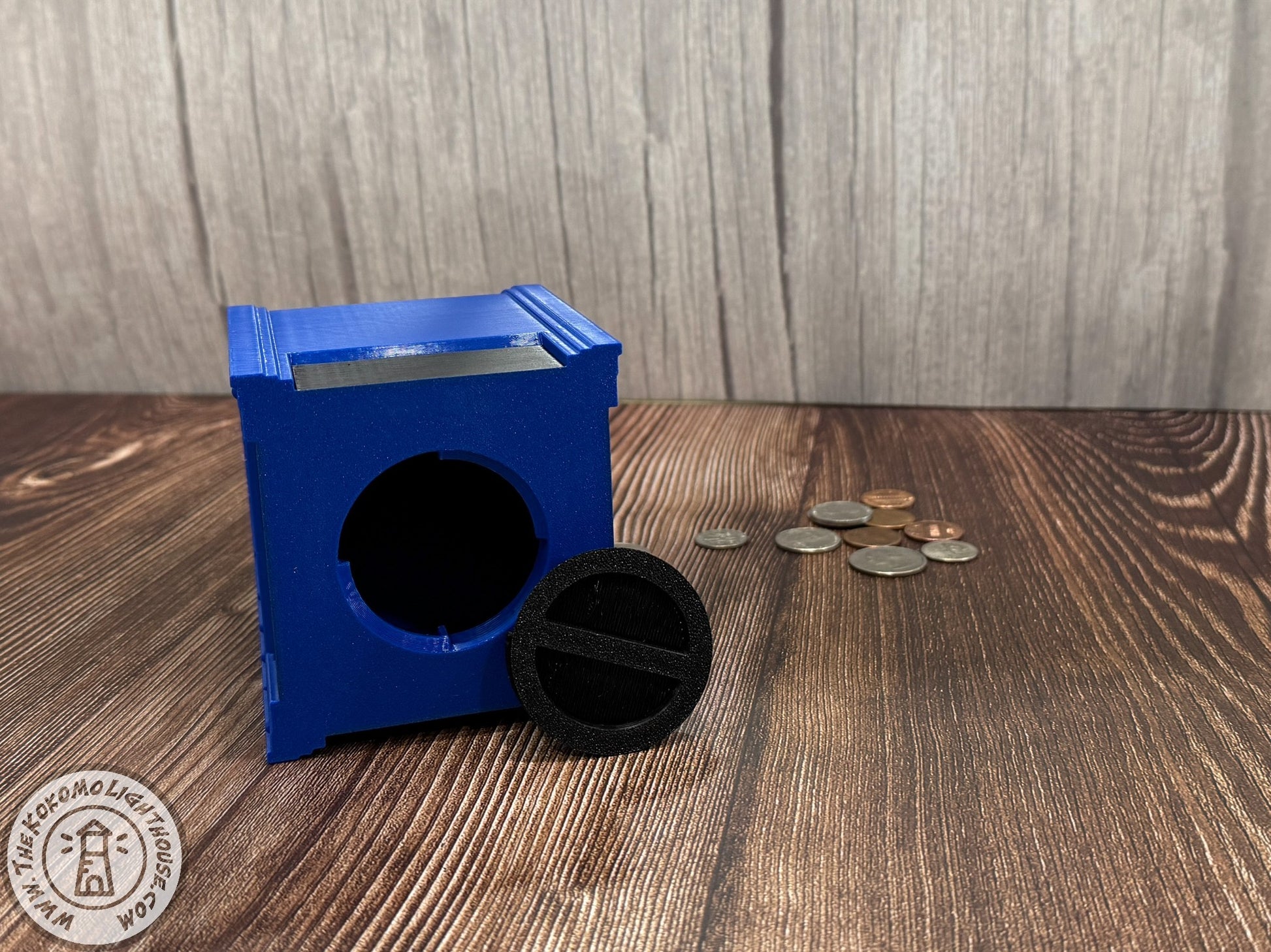 Blue mailbox piggy bank on its side with the coin removal plug removed on a wooden surface with coins around it