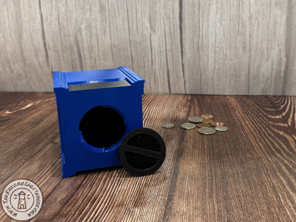 Blue mailbox piggy bank on its side with the coin removal plug removed on a wooden surface with coins around it