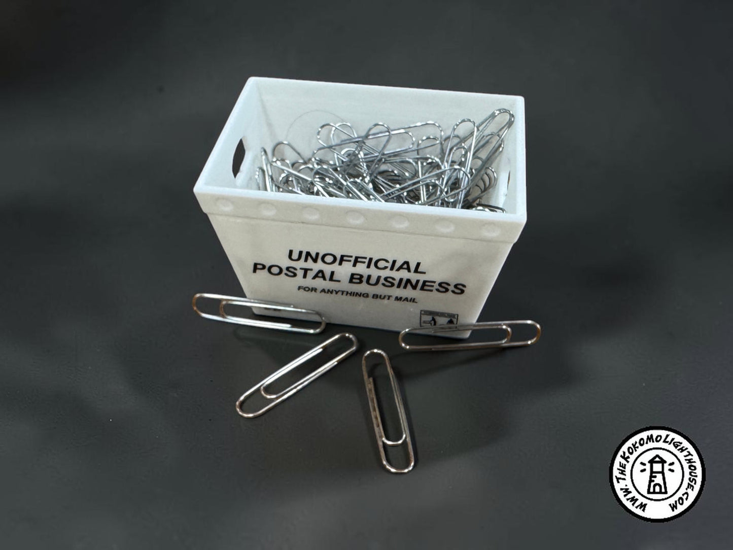 a miniature postal tub filled with paper clips, including some outside the tub on a dark background