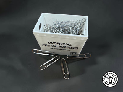 a miniature postal tub filled with paper clips, including some outside the tub on a dark background