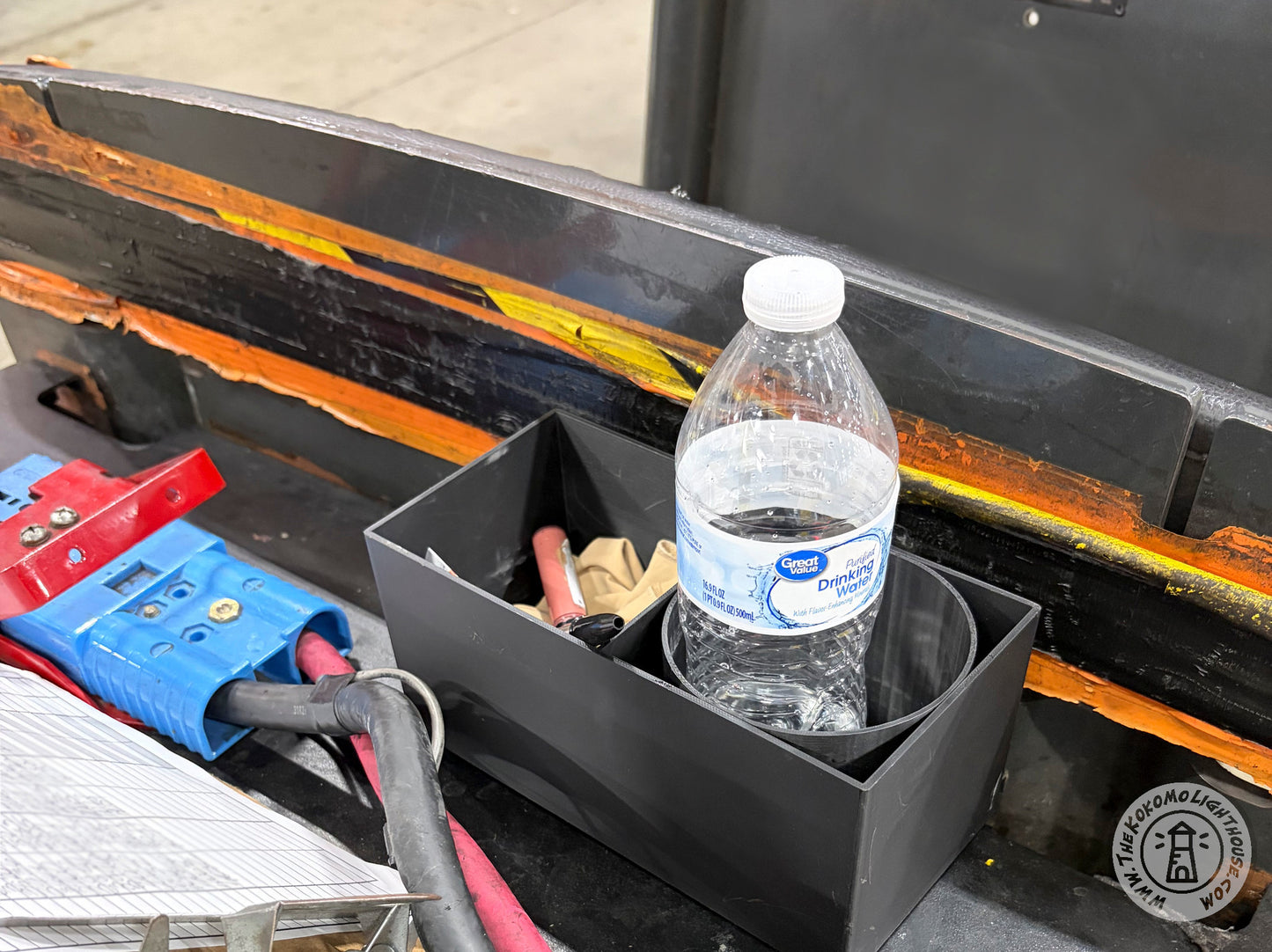 A caddy on the deck of a mo truck tugger holding a bottle of water and misc supplies.