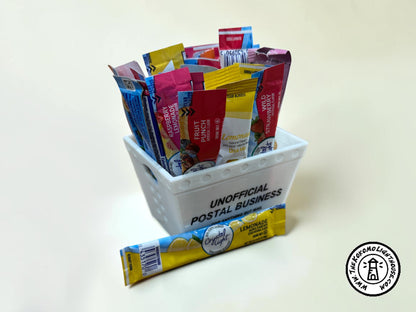 A mini postal tray filled with drink packets with one in front on a light background