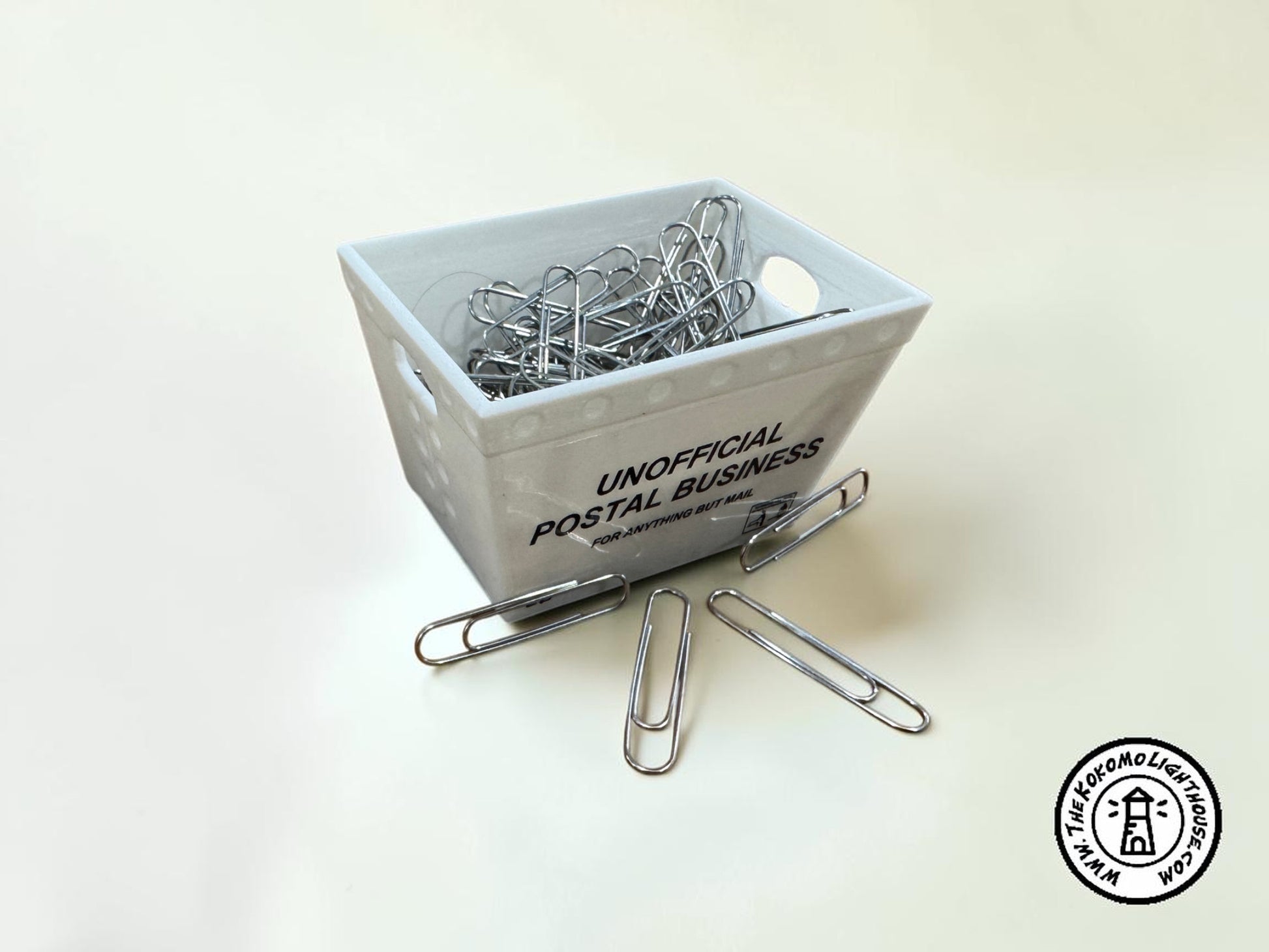 a miniature postal tub filled with paper clips, including some outside the tub on a light background