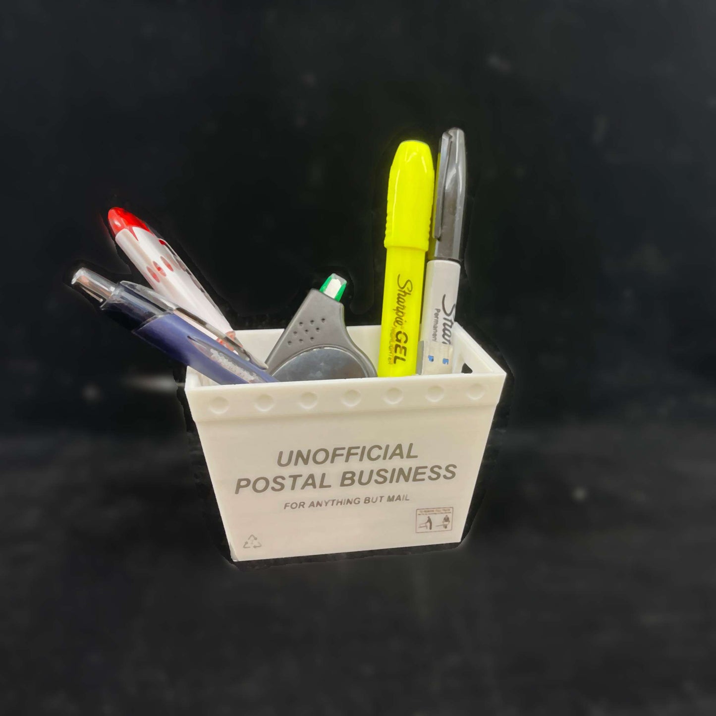 A small mini postal tub filled with office supplies including a highlighter, pens, and correction tape