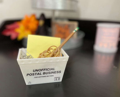 a mini mail tub filled with office supplies, including a pencil, rubber bands, paperclips, and sticky notes with a blurred background