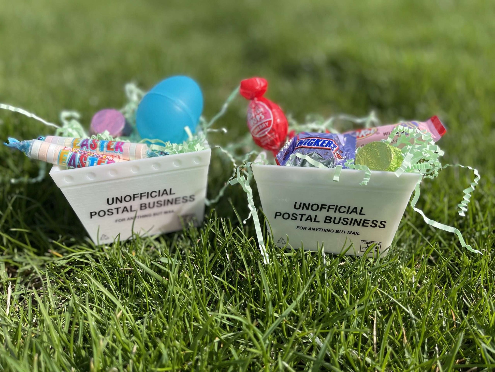 Two miniature postal trays filled with easter candy sitting on grass